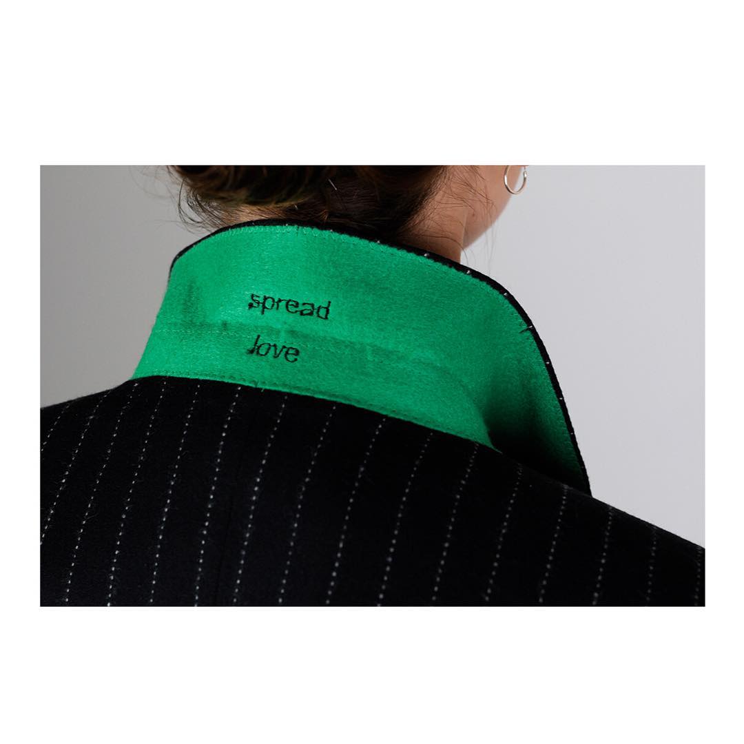 Spread love embroidered beneath a vivid green collar on a pinstriped jacket
