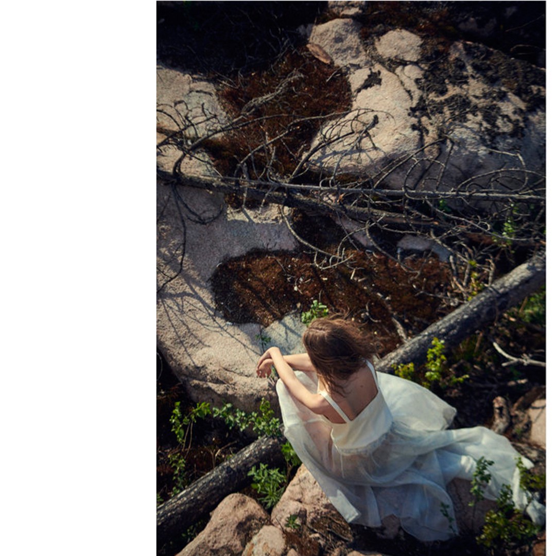 Overhead view of a woman in a flowing pale dress among rocks and fallen branches